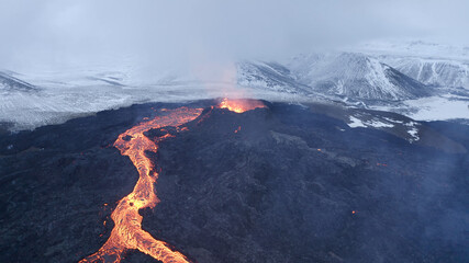 Fototapeta premium lava eruption volcano with snowy mountains, Aerial view Hot lava and magma coming out of the crater, April 2021 