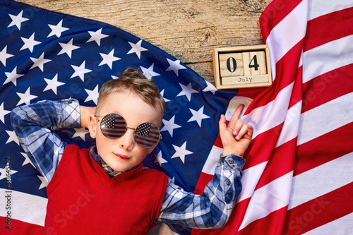 Cute and cheerful guy lying on a wooden background next to the American flag with glasses. Independence
