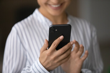 Close up smiling Indian woman holding smartphone in hands, having fun with gadget, happy young female browsing apps, chatting or shopping online, browsing apps, enjoying leisure time with phone