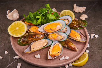 Fresh mussels in the sink lie on a large plate with parsley and lemon, on a dark gray table, sea salt is poured around the shells. The concept of healthy food and fresh seafood and delicacies.