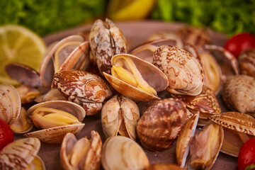 Fresh mussels in the vangole sink lie on a large plate on a dark gray table, surrounded by lettuce leaves, lemon and cherry tomatoes. The concept of healthy food and fresh seafood and delicacies.