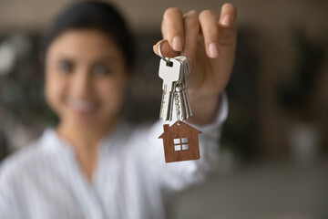 Close up focus on keys with keychain, excited tenant rejoicing relocation, satisfied customer purchasing new own apartment, Indian young woman excited by moving day, mortgage or rent concept