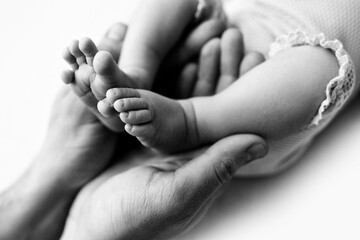 Feet of a newborn in the hands of a father, parent. Studio photography, black and white. Happy family concept.