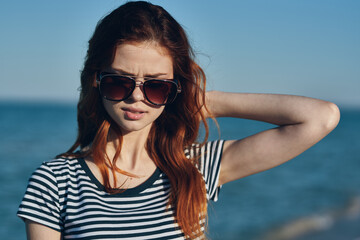 red-haired woman model in t-shirt and in sunglasses sea in the background summer vacation