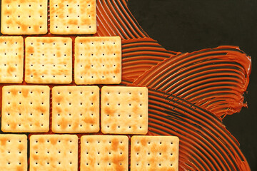 crackers and chocolate paste on black background, cookies lined up like brickwork or ceramic tiles, copy space for banner, culinary creative concept