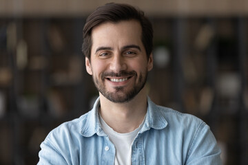 Head shot portrait smiling confident millennial man looking at camera, standing at home, happy...