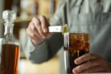 A professional bartender decorates the cocktail with lime. The bartender prepares a cocktail with whiskey and Cola. Preparing cocktails at the bar.
