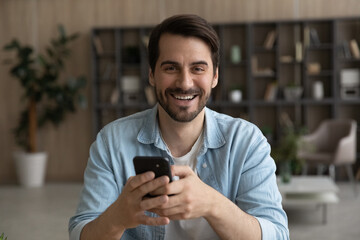 Head shot portrait laughing man holding smartphone, looking at camera, excited young male having...