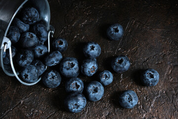 Blueberry berries spilled from metal bucket onto wooden table.