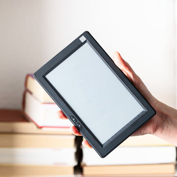 Hand  holding e-book  reader device against  the book closet with many book. Shallow of depth.