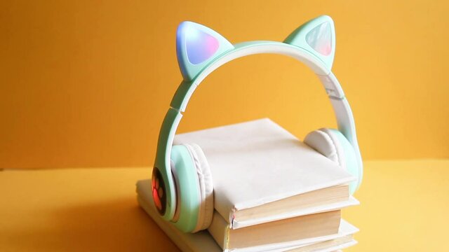 Audio fairy tales for children, audiobooks-a concept with children's headphones with cat ears, listening to stack paper books wrapped in white cover on yellow background. Education and entertainment.
