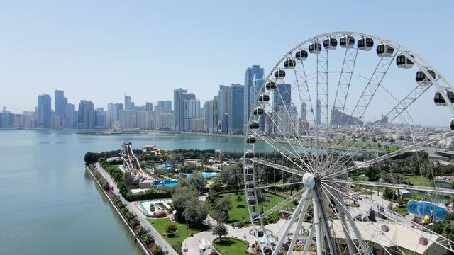 4K: Aerial view of Sharjah's Khalid Lake with city skyline and Eye of Emirates on a bright sunny day, United Arab Emirates