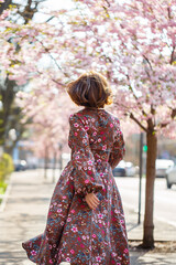 Beautiful young woman in a dress in blooming sakura trees. It's a spring warm sunny day outside