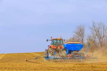 Obraz premium A farmer with a seeder on a tractor - sowing grain in an agricultural field. Growing wheat.