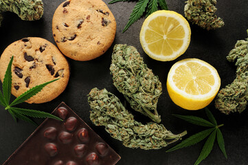 Sweets with CBD oil. Marijuana buds on black background. Cannabis flowers and chocolate cookies with nuts close-up. Top view, flat lay.