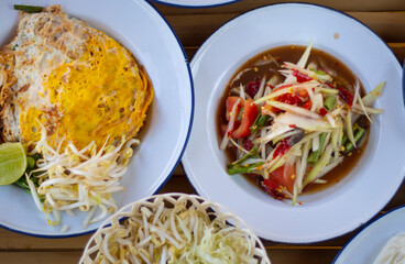 Papaya salad and Pad Thai, Thai style noodles on bamboo table, famous Thai food, som tam, green papaya, street food. Lao Southeast Asia, Isan region of Thailand.