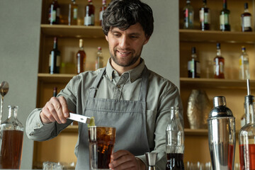A professional bartender decorates the cocktail with lime. The bartender prepares a cocktail with whiskey and Cola. Preparing cocktails at the bar.