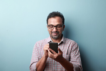 Middle aged man of Indian origin looking at his mobile phone with a smile - Powered by Adobe
