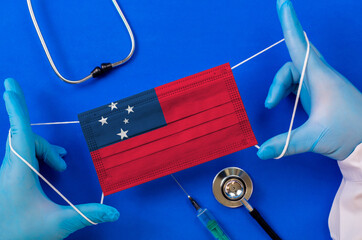 Medical mask with the flag of Samoa in the hands of a doctor and stethoscope, flat lay. Coronavirus...
