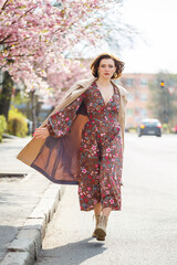 In the spring, a woman walks along a blooming street with sakura trees. A girl in a long silk elegant vintage dress walks among the flowering trees