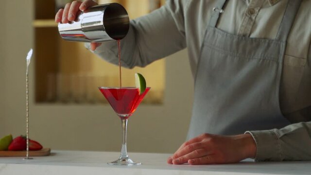 Bartender pouring Cosmopolitan cocktail in martini glass