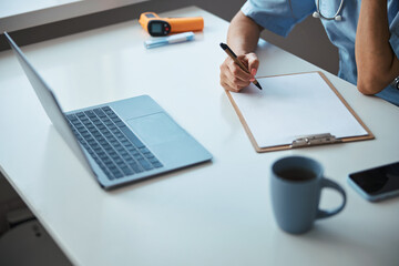 Female doctor using laptop and writing on clipboard clinic