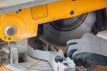 male hands of  construction worker sawing and cutting parts of  electric miter saw from  wooden board. wood board cutting process with blade rotation and dusty cloud electric miter saw