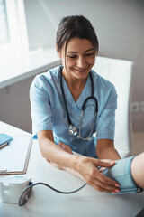 Joyful female doctor checking patient blood pressure in clinic