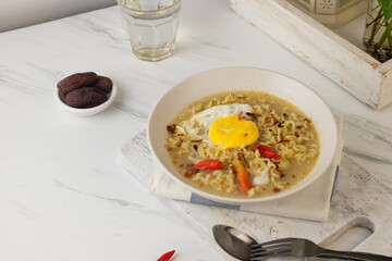 Mie Kuah Telur for Sahur in Ramadan, Instant noodle soup  served on white bowl with boiled pouch egg and chili.  White marble background. Copy space for text. 