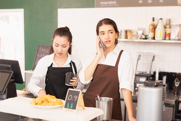 Caucasian barista woman confirms online orders with customer via mobile phone, Asian barista woman prepares takeaway coffee in cafe coffee shop