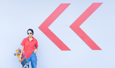 Asian cute girl or woman stand, hold skateboard, and act smart at cool wall with arrow in summer holiday