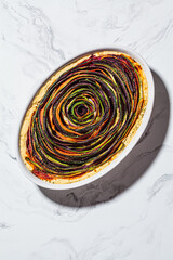 Baked vegetable tart spiral in white dish, top view. Healthy cooking concept.