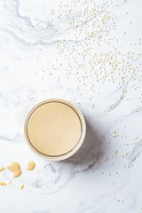 Sesame paste - tahini in glass jar, white marble background, top view. Israeli cuisine concept.