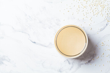 Sesame paste - tahini in glass jar, white marble background, top view. Israeli cuisine concept.