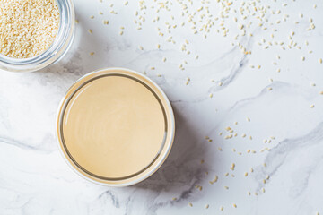 Sesame paste - tahini in glass jar, white marble background, top view. Israeli cuisine concept.