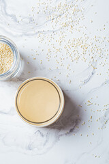Sesame paste - tahini in glass jar, white marble background, top view. Israeli cuisine concept.