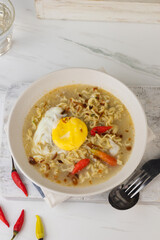 Mie Kuah Telur for Sahur in Ramadan, Instant noodle soup  served on white bowl with boiled pouch egg and chili.  White marble background. Copy space for text. 