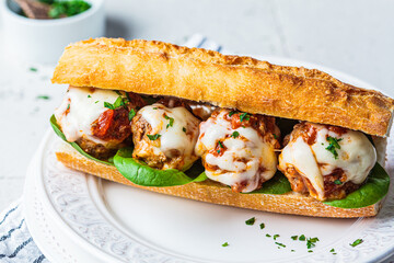 Sub meatballs sandwich with cheese and tomato sauce in baguette on white plate.