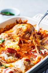 Closeup of baked cheesy meatballs casserole with tomato sauce in the oven dish.