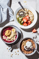 Flat lay of assorted oatmeal bowls with chocolate, fruit, berry and yogurt, gray tiles background, top view. Healthy breakfast concept.