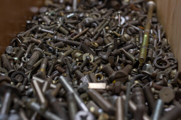 a pile of dirty old bolts nuts screws washers of different sizes lie in a heap in a wooden box in a workshop