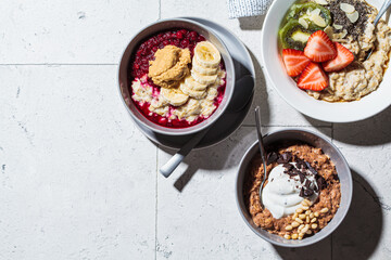 Oatmeal bowls with chocolate, fruit, peanut butter and yogurt, gray tiles background, copy space. Healthy breakfast concept.