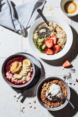 Flat lay of assorted oatmeal bowls with chocolate, fruit, berry and yogurt, gray tiles background, top view. Healthy breakfast concept.