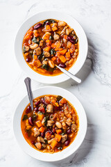 Flat lay of italian beans soup with sausages in white plate, top view, white marble background.