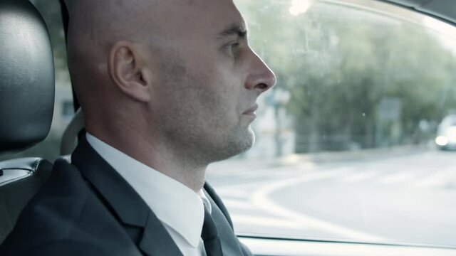 Profile of middle-aged bold man in official suit driving car. Handheld shot of serious Caucasian driver looking at road. Sun rays entering auto. Business, transport, occupation concept