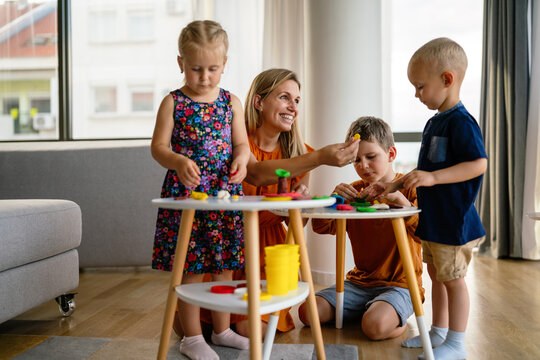 Mother or nursery teacher teaches her children to work with colorful play clay toys