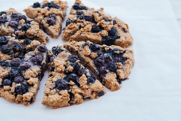 Freshly baked oat blueberry scones on baking paper on white wooden background. Sweet food with natural ingredients. Vegan gluten free pastry.