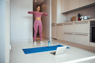 Cheerful sporty woman using laptop and doing exercise at home