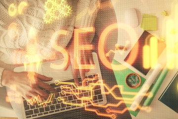 Double exposure of woman hands working on computer and SEO hologram drawing. Top View. Search optimization concept.