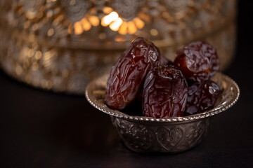 Religious Islamic festival and holy month of Ramadan, EID KAREEM, concept: Close up on a metallic bowl with dried date fruits and a golden lantern with candle light on dark background with copy space